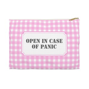Könnte beinhalten: Ein rosa-weiß kariertes Reißverschlussetui mit dem Text "OPEN IN CASE OF PANIC" in einem gerahmten Etikett. Die Tasche hat einen goldfarbenen Reißverschluss.