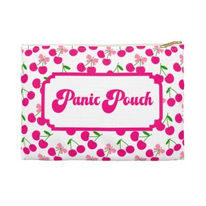 Puede incluir: Una bolsa blanca con cremallera con un estampado de cerezas rosas y las palabras "Panic Pouch" en un marco rosa. Las cerezas tienen tallos verdes y lazos rosas. La cremallera es dorada.
