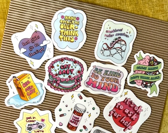 May include: A set of 11 colorful stickers with various phrases and illustrations. The stickers feature phrases like "Hang on,  I'll think this over", "Real men cry", "Be kind to your mind", "It's ok to ask for help", and "Great minds don't think alike". The stickers are perfect for adding a touch of personality to laptops, water bottles, journals, and more.