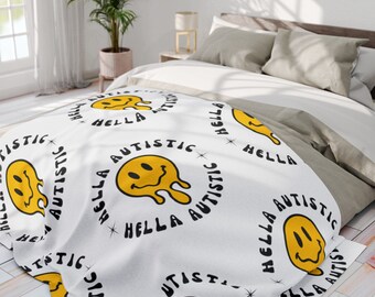 May include: White throw blanket with a repeating pattern of yellow smiley faces with dripping yellow paint and the text "hella autistic" in black.