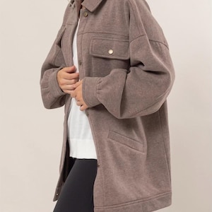 Puede incluir: Una chaqueta de forro polar marrón de gran tamaño con cierre de botones, dos bolsillos grandes y mangas largas.