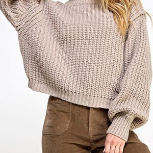 K&ouml;nnte beinhalten: Ein beiger Strickpullover mit Rundhalsausschnitt und langen &Auml;rmeln. Der Pullover hat eine lockere Passform und eine leicht verk&uuml;rzte L&auml;nge.