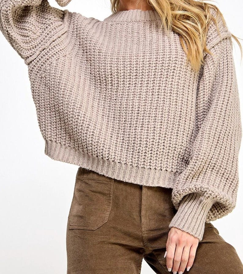 K&ouml;nnte beinhalten: Ein beiger Strickpullover mit Rundhalsausschnitt und langen &Auml;rmeln. Der Pullover hat eine lockere Passform und eine leicht verk&uuml;rzte L&auml;nge.