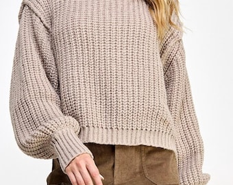 May include: A light brown, chunky knit jumper with long sleeves and a round neckline.