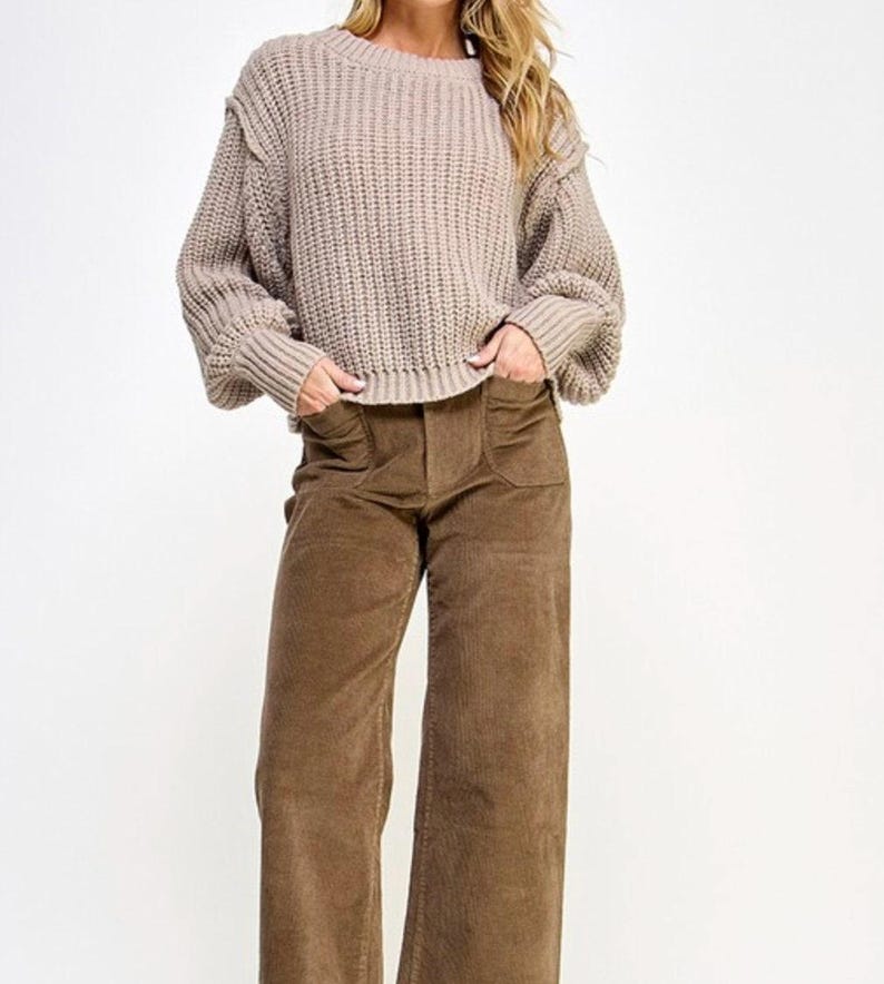 K&ouml;nnte beinhalten: Ein hellbrauner Strickpullover mit Rundhalsausschnitt und langen &Auml;rmeln. Der Pullover hat eine leicht verk&uuml;rzte L&auml;nge und eine lockere Passform.