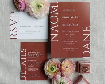 May include: Wedding invitation suite featuring a terracotta-colored invitation card with white text, RSVP card, and details card. The invitation includes the names Naomi Adler and Dane Powell, date, and location. Pink and yellow flowers and ring boxes are also present.