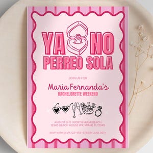 Pode incluir: Um convite rosa para despedida de solteira com o texto "YA NO PERREO SOLA" e "Maria Fernanda's BACHELORETTE WEEKEND". O convite inclui ilustrações de um anel, taças de champanhe e óculos de sol. O convite está em um prato de madeira.