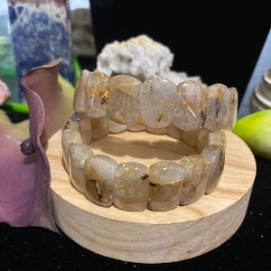 Pode incluir: Duas pulseiras empilhadas feitas de quartzo transparente com inclusões douradas e pretas. As pulseiras são feitas de contas retangulares.