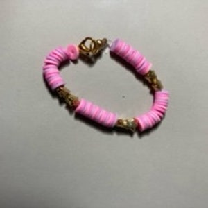 Può includere: Un braccialetto di perline rosa con dettagli dorati. Il braccialetto è fatto di piccole perline rotonde e ha una chiusura a scatto.