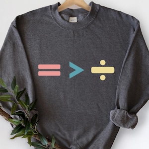 Può includere: Felpa grigio scuro con un design grafico con un segno uguale rosa, un segno maggiore di turchese e un simbolo di divisione giallo. La felpa ha un girocollo.