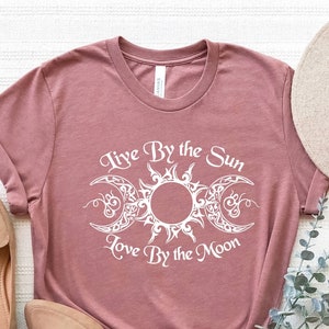 May include: A mauve t-shirt with a white graphic of a sun and moon with the text "Live By the Sun Love By the Moon".