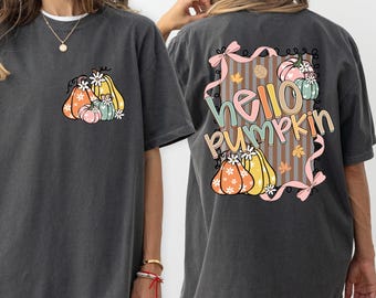 May include: Dark gray t-shirt with a pumpkin graphic on the front pocket and back. The back of the shirt features the text "Hello Pumpkin" with pumpkins and fall leaves. The shirt is a comfortable, oversized fit.
