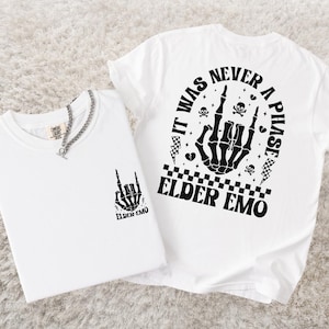 K&ouml;nnte beinhalten: Zwei wei&szlig;e T-Shirts mit schwarzen Grafikdesigns. Ein Shirt zeigt eine Skeletthand, die eine Rock'n'Roll-Geste macht, mit dem Text "ELDER EMO" darunter. Das andere Shirt hat den Text "IT WAS NEVER A PHASE" und eine Skeletthand.