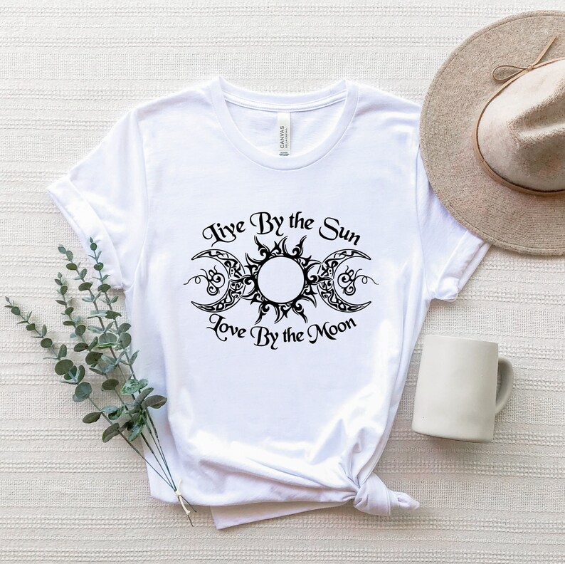 May include: White t-shirt with a black graphic of a sun and moon with the text "Live By the Sun Love By the Moon".