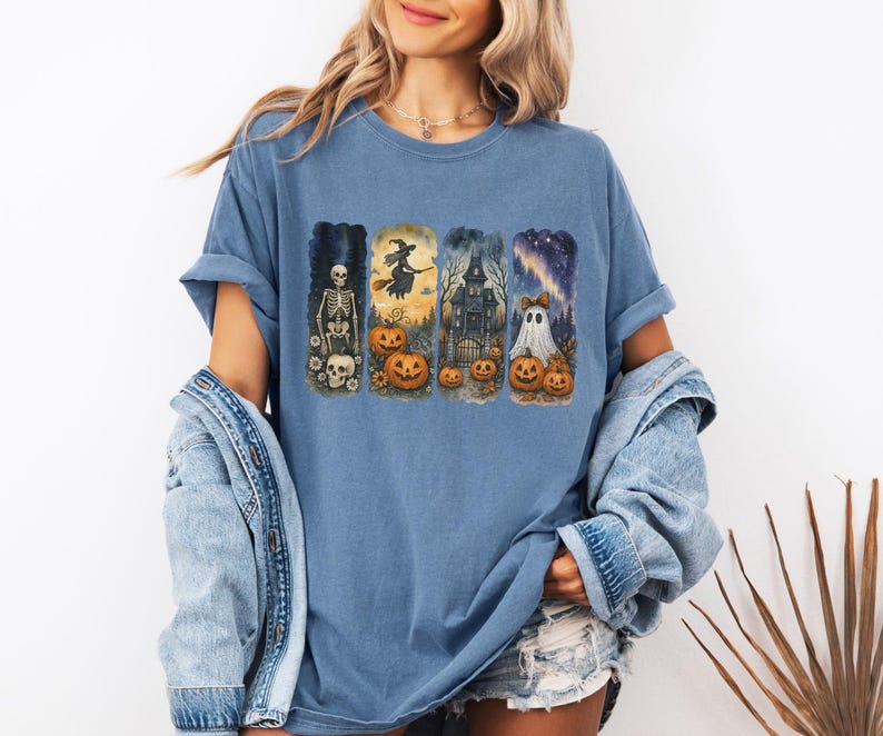 May include: A blue t-shirt featuring a Halloween-themed design. The graphic includes a skeleton, witch, haunted house, and ghost, each with pumpkins. The shirt has short sleeves and a relaxed fit.