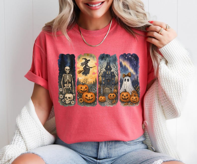 May include: Coral-colored t-shirt featuring four Halloween-themed illustrations. The designs include a skeleton, a witch on a broom, a haunted house, and a ghost with pumpkins. The artwork is in a watercolor style.