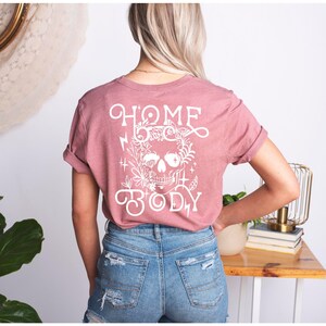 May include: A pink t-shirt with a white skull design and the text "HOME BODY" on the back.