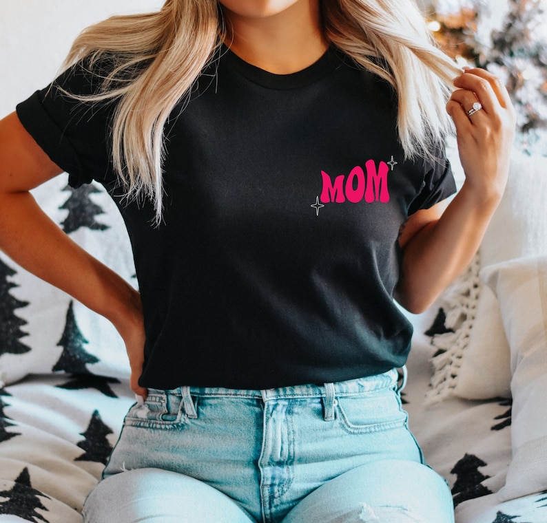 Puede incluir: Una camiseta negra con un gr&aacute;fico rosa de "MOM" en la parte delantera. La camiseta tiene un corte holgado y est&aacute; hecha de una tela suave y c&oacute;moda.