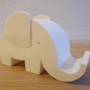 May include: White ceramic elephant phone stand. The elephant has a large trunk that curves up and around to form a phone holder.