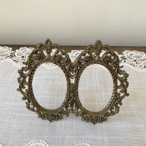 May include: Ornate, antique-style double oval picture frame in a bronze finish. The frame features intricate scrollwork and floral details, perfect for displaying two cherished photos. A decorative piece for home decor.