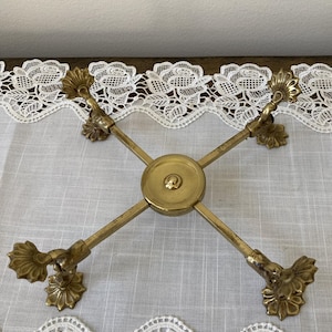 May include: A vintage brass decorative stand with a cross-shaped design. The stand features ornate floral accents at the ends of each arm and a central circular plate. The brass has a warm, aged patina.