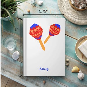 May include: White notebook with a red, blue, and orange maraca design. The notebook is 8 inches tall and 5.75 inches wide. The name "Emily" is printed on the front of the notebook.