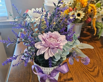 May include: A purple and white striped ceramic vase with a purple ribbon bow holds a bouquet of lavender, eucalyptus, and a single pink dahlia.