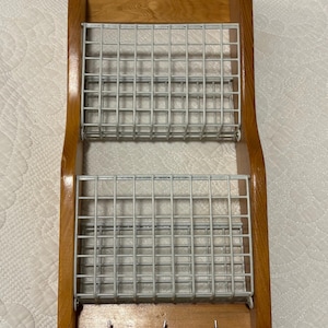 May include: A wooden wall-mounted organizer with two wire mesh baskets and three key hooks. The wood has a warm, light brown finish. The wire mesh is a light gray color. The organizer is designed for home organization.