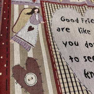 May include: A woven throw blanket with a patchwork design. The blanket features a heart with a button, an angel, and the text "Good Friends are like you don't have to see..." in black lettering. The color palette includes burgundy, beige, and purple.
