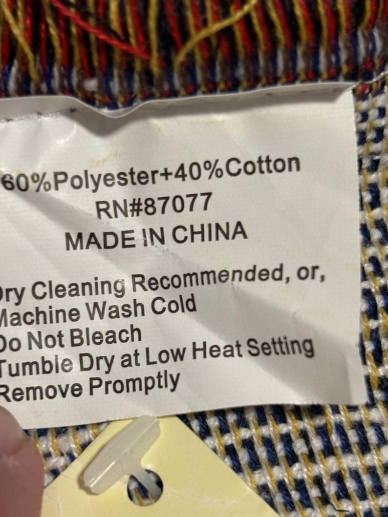 May include: A white tag with black text indicating the composition of a textile: 60% Polyester and 40% Cotton. The tag also states "MADE IN CHINA" and care instructions: dry cleaning or machine wash cold.