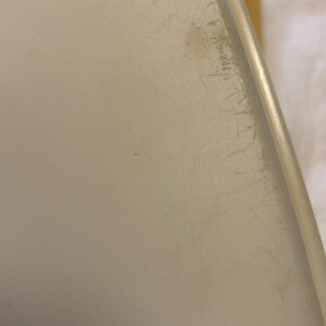 Pu&ograve; includere: Primo piano di una superficie bianco sporco, forse plastica, con graffi e imperfezioni visibili. Il bordo dell'oggetto &egrave; arrotondato e ha un aspetto pi&ugrave; chiaro, quasi traslucido. Il tono generale &egrave; neutro.