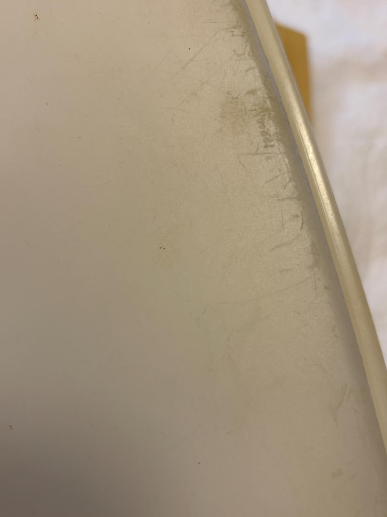 Pu&ograve; includere: Primo piano di una superficie bianco sporco, forse plastica, con graffi e imperfezioni visibili. Il bordo dell'oggetto &egrave; arrotondato e ha un aspetto pi&ugrave; chiaro, quasi traslucido. Il tono generale &egrave; neutro.