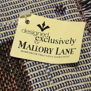 May include: Close-up of a woven fabric with a tag attached. The fabric has a blue, white, and black checkered pattern with red accents. The tag reads "designed exclusively for MALLORY LANE HOME DECOR THAT'S JUST YOUR STYLE."
