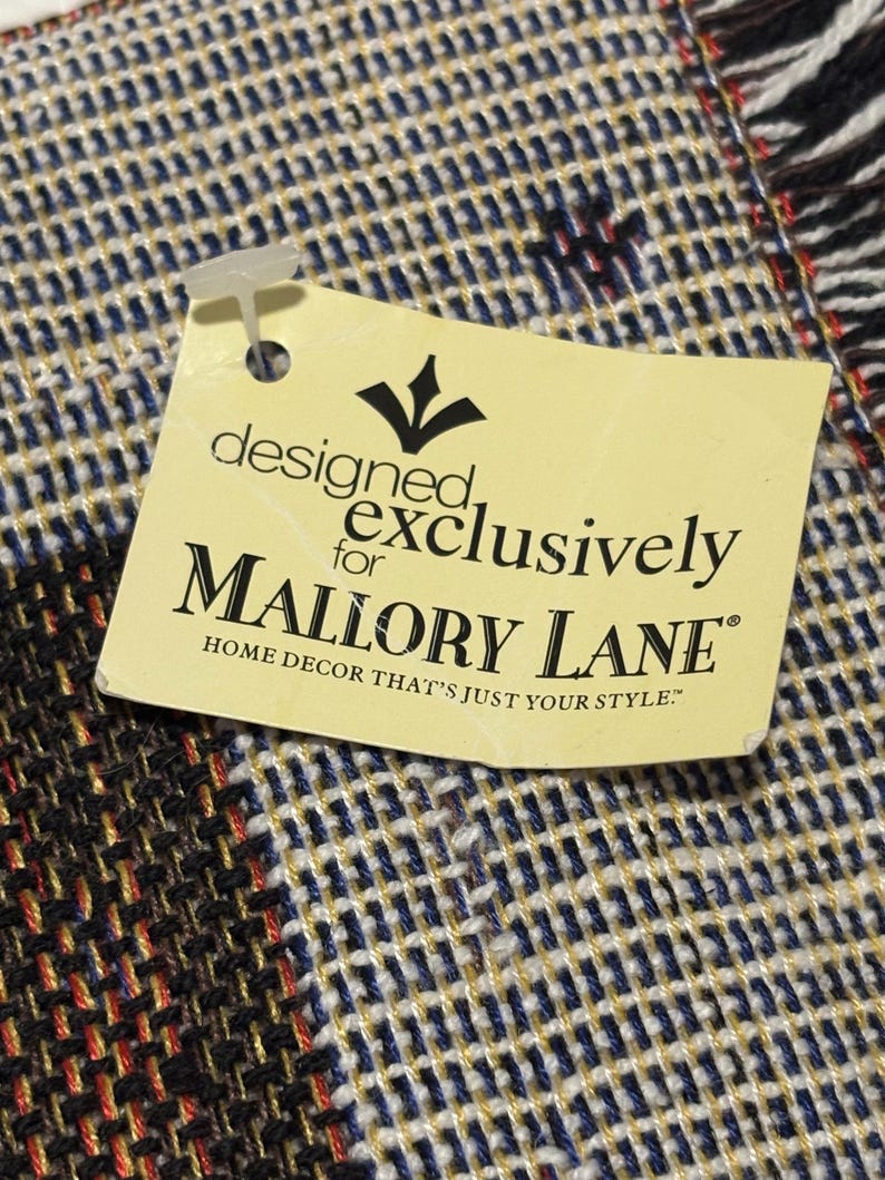 May include: Close-up of a woven fabric with a tag attached. The fabric has a blue, white, and black checkered pattern with red accents. The tag reads "designed exclusively for MALLORY LANE HOME DECOR THAT'S JUST YOUR STYLE."