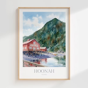 May include: A framed watercolor print depicting a red building on stilts labeled Icy Strait Point Alaska, set against a large green mountain and a rocky shoreline. The water reflects the scene, and the text HOONAH ALASKA appears at the bottom.