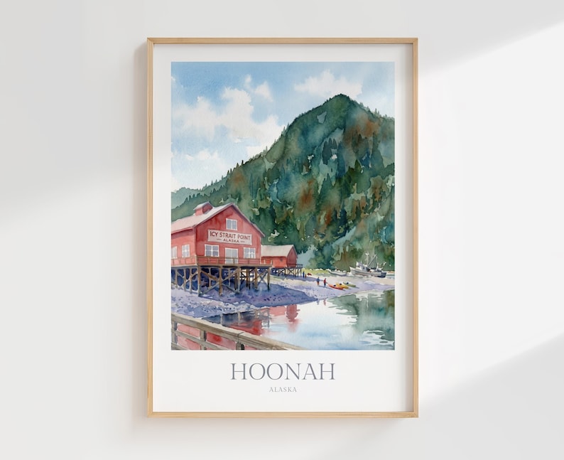 May include: A framed watercolor print depicting a red building on stilts labeled Icy Strait Point Alaska, set against a large green mountain and a rocky shoreline. The water reflects the scene, and the text HOONAH ALASKA appears at the bottom.