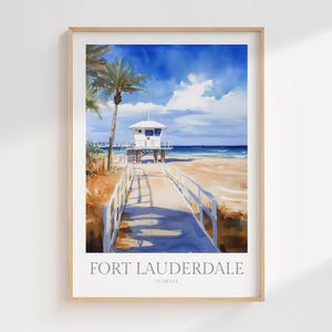 May include: A framed art print featuring a watercolor illustration of a beach scene in Fort Lauderdale, Florida. The image depicts a wooden boardwalk leading toward a white lifeguard tower, palm trees, sandy dunes, and a bright blue sky.