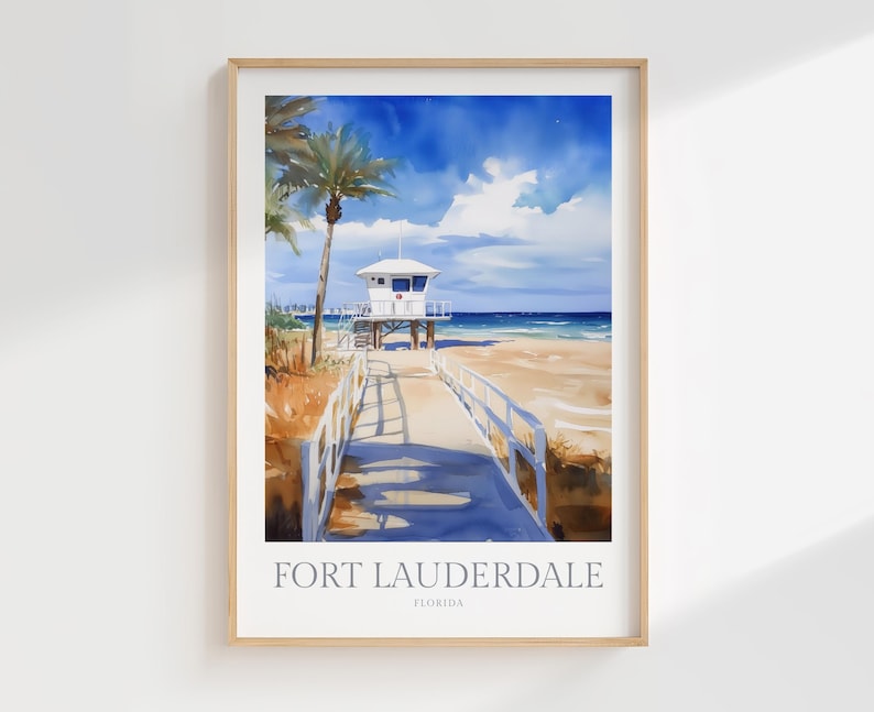 May include: A framed art print featuring a watercolor illustration of a beach scene in Fort Lauderdale, Florida. The image depicts a wooden boardwalk leading toward a white lifeguard tower, palm trees, sandy dunes, and a bright blue sky.