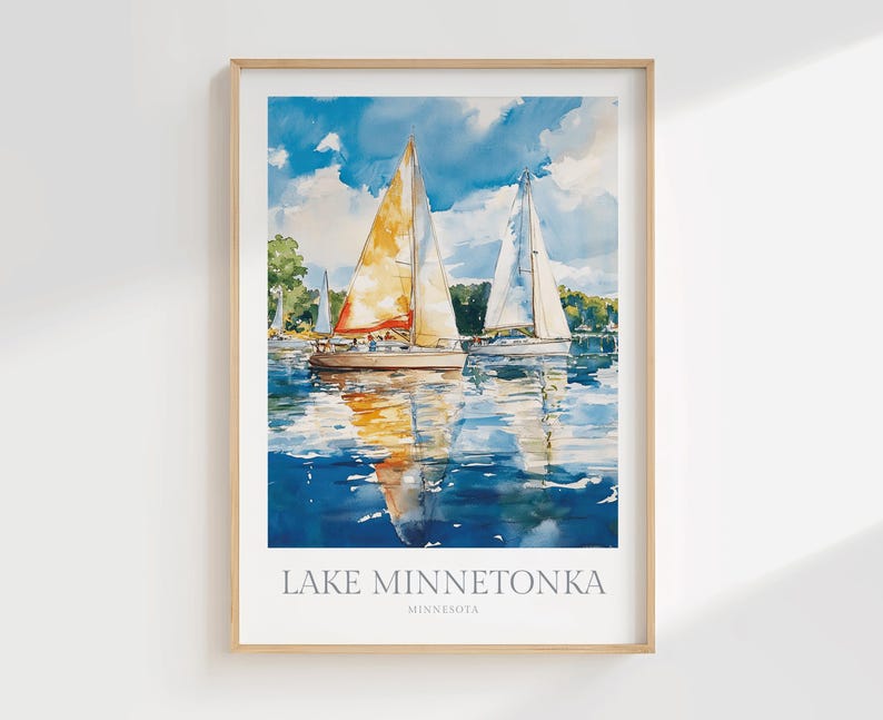 May include: A framed watercolor art print featuring two sailboats on blue water under a cloudy sky. The primary sailboat has a large orange and yellow sail. The text at the bottom reads LAKE MINNETONKA MINNESOTA in a clean, sans-serif font.