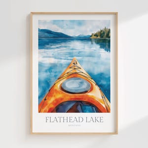 May include: A framed art print featuring a watercolor illustration of an orange kayak on blue water, with mountains and trees in the distance. The text at the bottom reads FLATHEAD LAKE MONTANA in a clean, sans-serif font against a white background.
