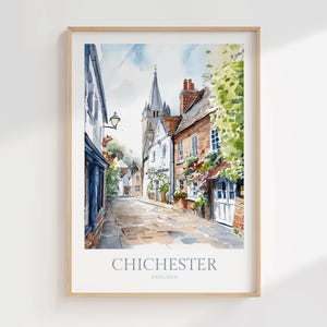 May include: A watercolor print of a street scene in Chichester, England, featuring historic brick and white buildings, a tall church spire in the distance, and lush green foliage. The text CHICHESTER ENGLAND is printed at the bottom of the frame.