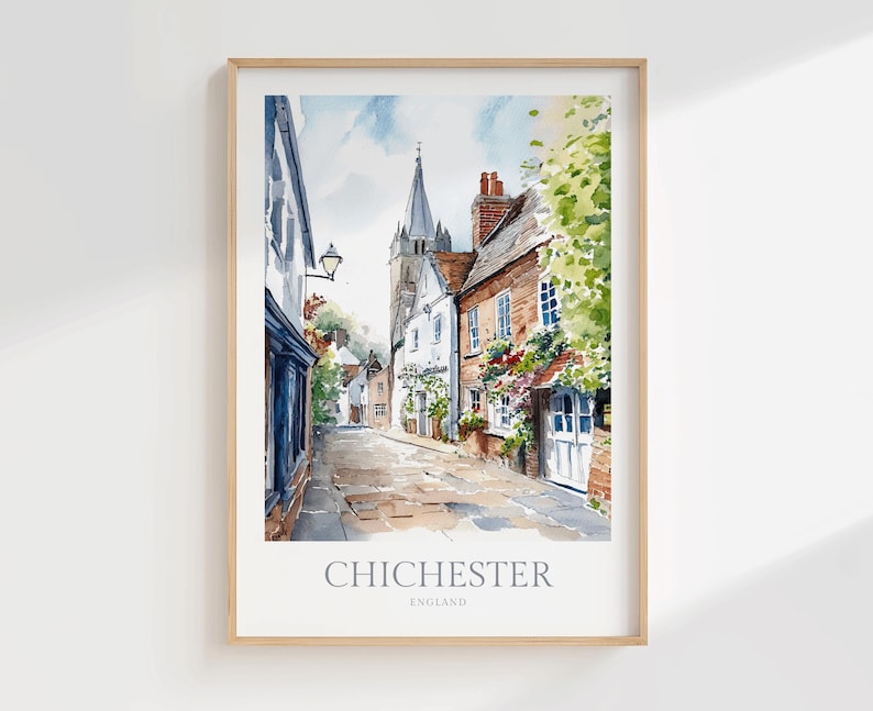 May include: A watercolor print of a street scene in Chichester, England, featuring historic brick and white buildings, a tall church spire in the distance, and lush green foliage. The text CHICHESTER ENGLAND is printed at the bottom of the frame.