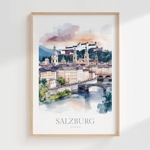 May include: Watercolour print of Salzburg, Austria, depicting a cityscape with buildings, bridges, and a river. The artwork uses a soft colour palette with shades of blue, beige, and orange. The word "SALZBURG" is printed at the bottom.