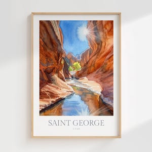 May include: A framed watercolor print depicting a narrow canyon with towering red rock walls, a flowing stream reflecting the blue sky, and a bright sunburst. The text at the bottom reads SAINT GEORGE UTAH in a clean, sans-serif font.