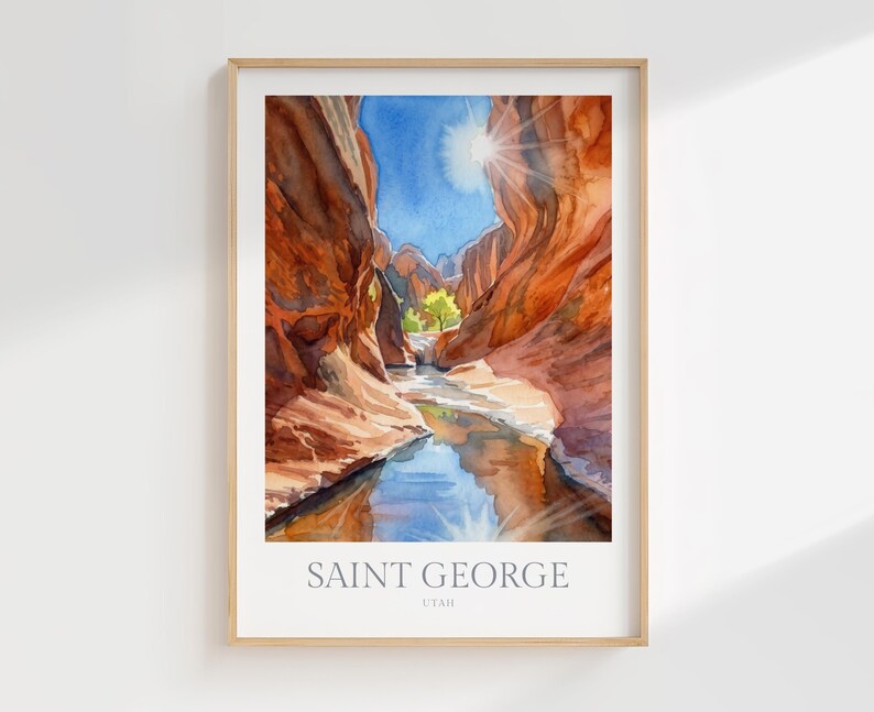 May include: A framed watercolor print depicting a narrow canyon with towering red rock walls, a flowing stream reflecting the blue sky, and a bright sunburst. The text at the bottom reads SAINT GEORGE UTAH in a clean, sans-serif font.