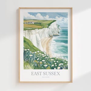Puede incluir: Impresión en acuarela enmarcada de la costa de East Sussex, Inglaterra, con acantilados blancos, campos verdes y el mar. El texto "EAST SUSSEX ENGLAND" está impreso en la parte inferior.