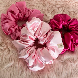 May include: Three satin scrunchies in pink and fuchsia shades. The scrunchies are made of soft, silky fabric and are perfect for holding hair in place.