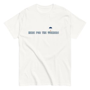 Può includere: T-shirt bianca con la scritta "HERE FOR THE WIENERS" in lettere blu. Una piccola grafica di paracadute blu è sopra il testo. La maglietta è realizzata in un materiale morbido e ha maniche corte.