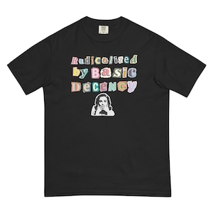 Puede incluir: Camiseta negra con el texto "Radicalized by Basic Decency" en letras coloridas de estilo recortado. Debajo, un gráfico en blanco y negro de una mujer cubriéndose la boca. La camiseta es de estilo casual.