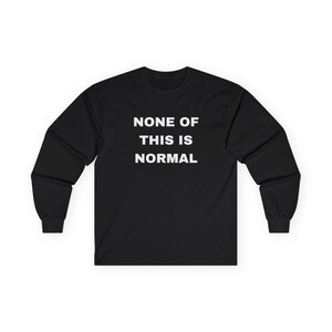 May include: Black long-sleeved shirt featuring the white text "NONE OF THIS IS NORMAL". The shirt has a crew neck and long sleeves. The text is in a bold, sans-serif font.